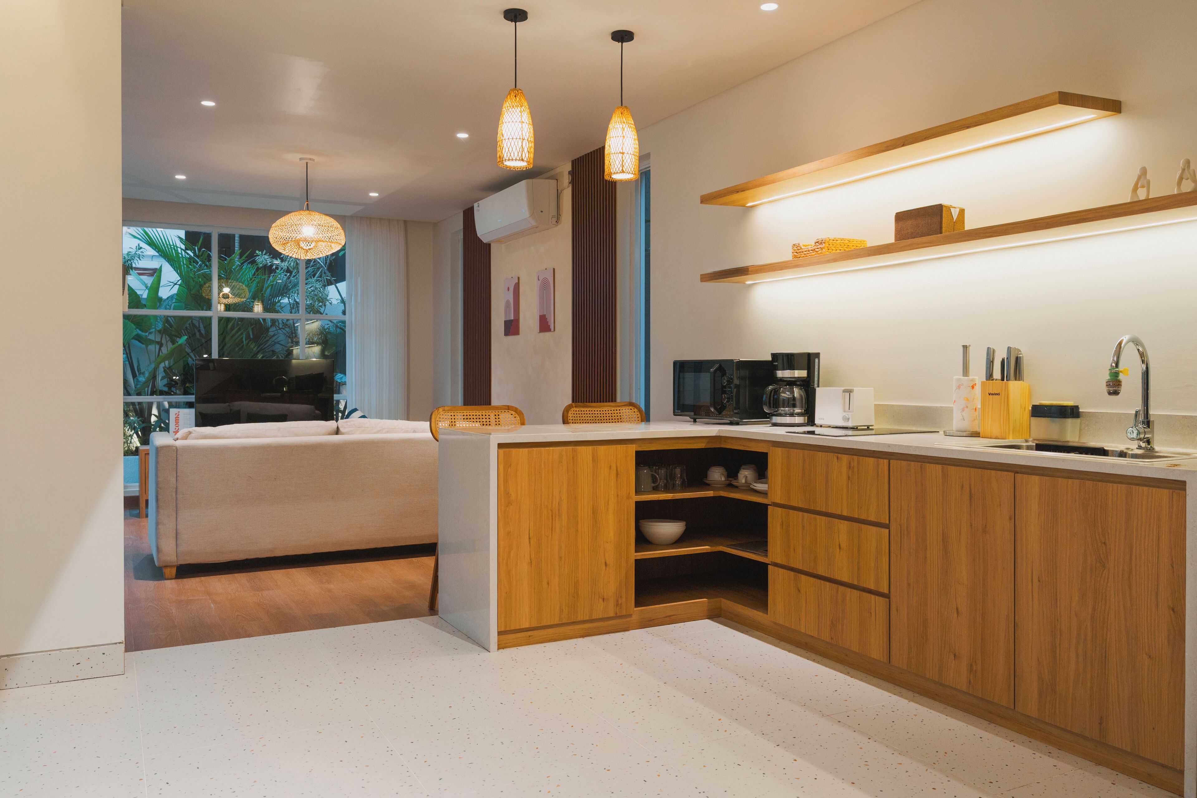 A modern kitchen with wooden cabinets, a built-in island, pendant lighting, and a view of the outdoors.
