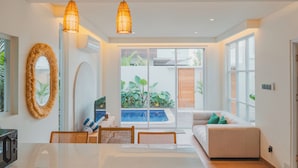 A modern living room with a large window, a dining area, and a pool view. - Uma Avaya Villas Canggu (Canggu)