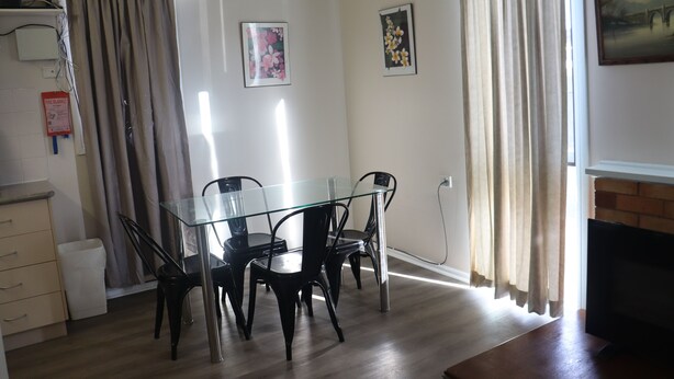 A dining area with a glass table and black chairs, a fire alarm on the wall, and a fireplace. - The Sundown Stay (Dubbo)