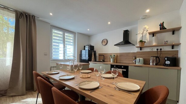 A modern kitchen with a wooden dining table set for four, equipped with wine glasses and plates.