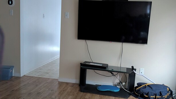 Une pièce avec un téléviseur à écran plat fixé au mur, une petite table avec un tapis, un sac bleu et une porte donnant sur une autre pièce.