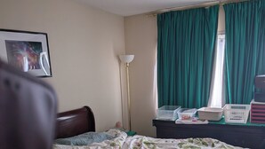 Une chambre à coucher comprenant un lit, une table de chevet, une lampe, une fenêtre avec des rideaux et un tableau accroché au mur.