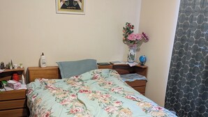 Une chambre à coucher avec une couvre-lit à motifs floraux, une tête de lit en bois, une table de chevet sur laquelle repose un globe terrestre, un vase rempli de fleurs et un tableau encadré accroché au mur.