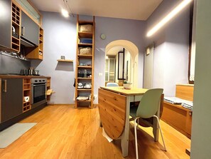 A compact kitchen with wooden cabinets, a built-in oven, and a wooden dining table with a chair. - The Heart of Rome (Roma)