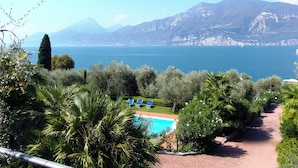 A pool area with lounge chairs, surrounded by lush greenery and overlooking a body of water with mountains in the background. - Casa Pagani  (Brenzone sul Garda)