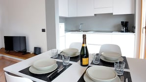 A modern kitchen with white cabinets, a black countertop, and a dining table set with plates, glasses, and a bottle of champagne. - Casa Pagani  (Brenzone sul Garda)