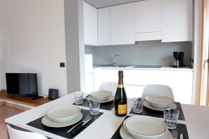 A modern kitchen with white cabinets, a black countertop, and a dining table set with plates, glasses, and a bottle of champagne. - Casa Pagani  (Brenzone sul Garda)