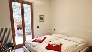 A bedroom with a bed, a radiator, a chair, and a view of a stone wall through a glass door. - Casa Pagani  (Brenzone sul Garda)