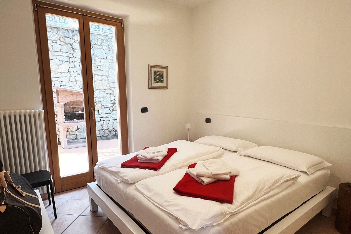 A bedroom with a bed, a radiator, a chair, and a view of a stone wall through a glass door.