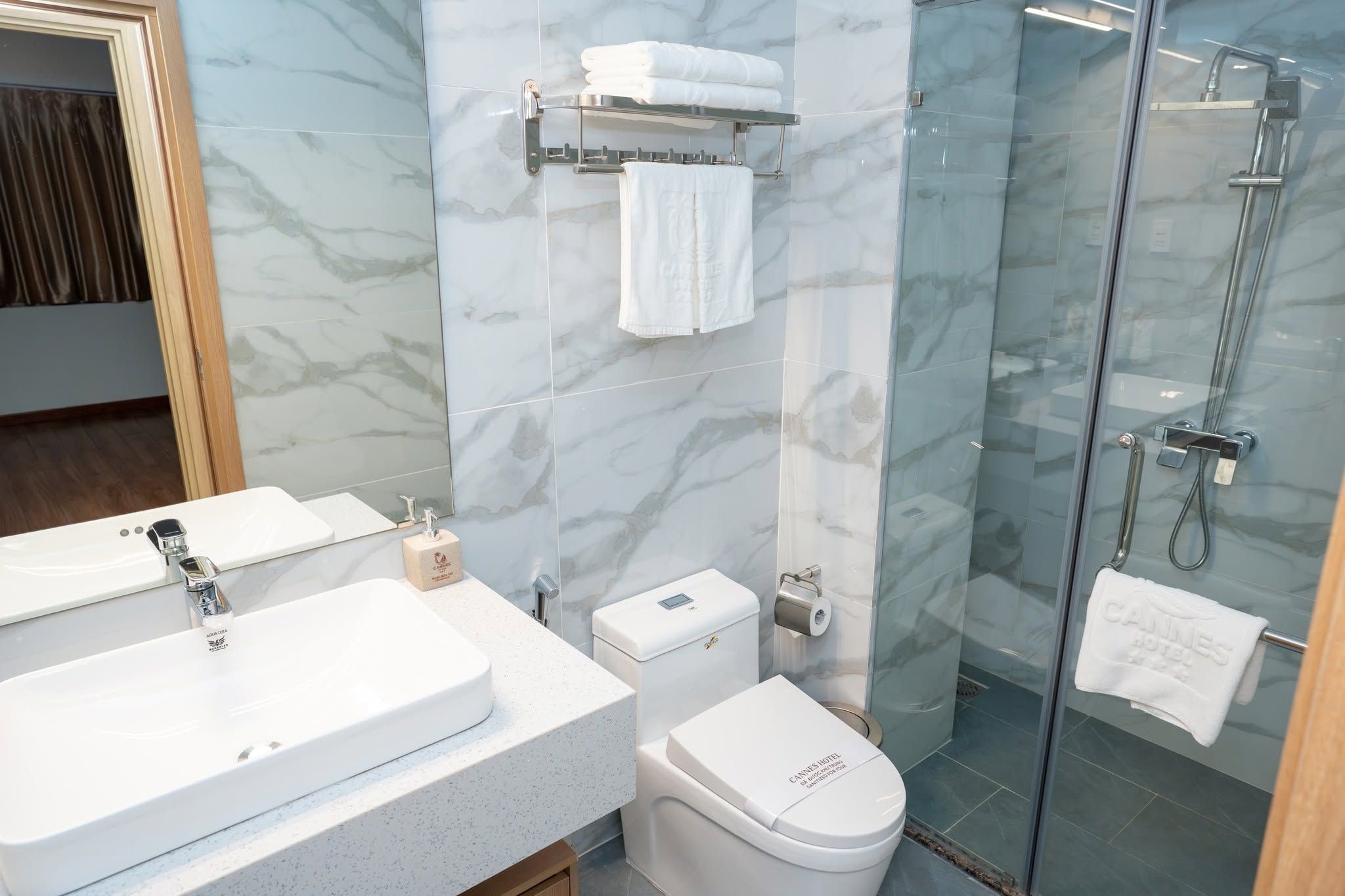 A bathroom with a marble wall, a glass shower enclosure, a white sink, and a toilet.