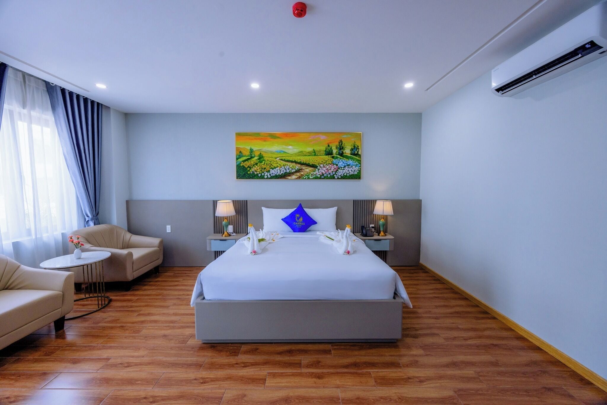 Una habitación de hotel con una cama grande, dos mesitas de noche, un sillón y un cuadro en la pared.