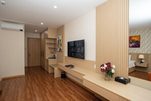 A modern hotel room with a wooden floor, a reception desk, a large abstract painting, and a bed with a nightstand. - Cannes Hotel (Phu Khuong)
