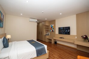 A hotel room with a bed, bedside table, lamp, artwork, TV, and a wooden cabinet. - Cannes Hotel (Phu Khuong)