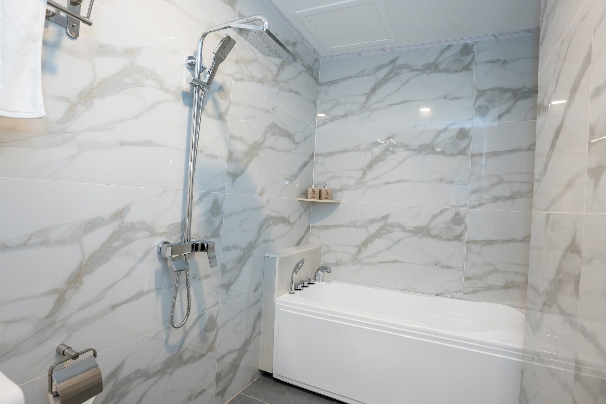 A modern bathroom with a shower, a bathtub, and marble walls.