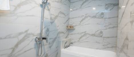 A modern bathroom with a shower, a bathtub, and marble walls.