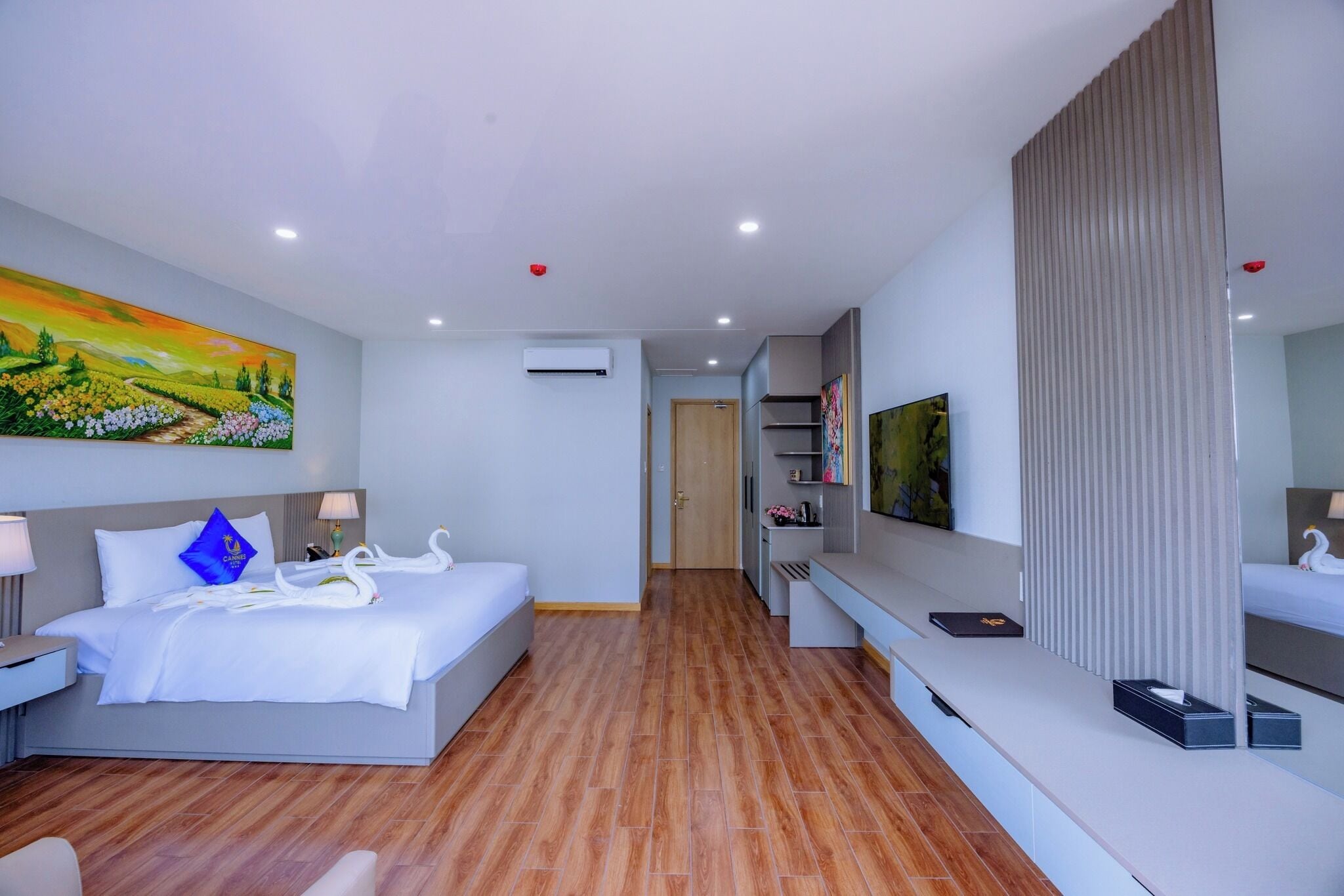 A modern hotel room with a large bed, a flat-screen TV, a desk, and a painting on the wall.