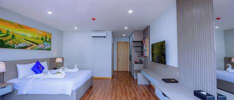 A modern hotel room with a large bed, a flat-screen TV, a desk, and a painting on the wall.