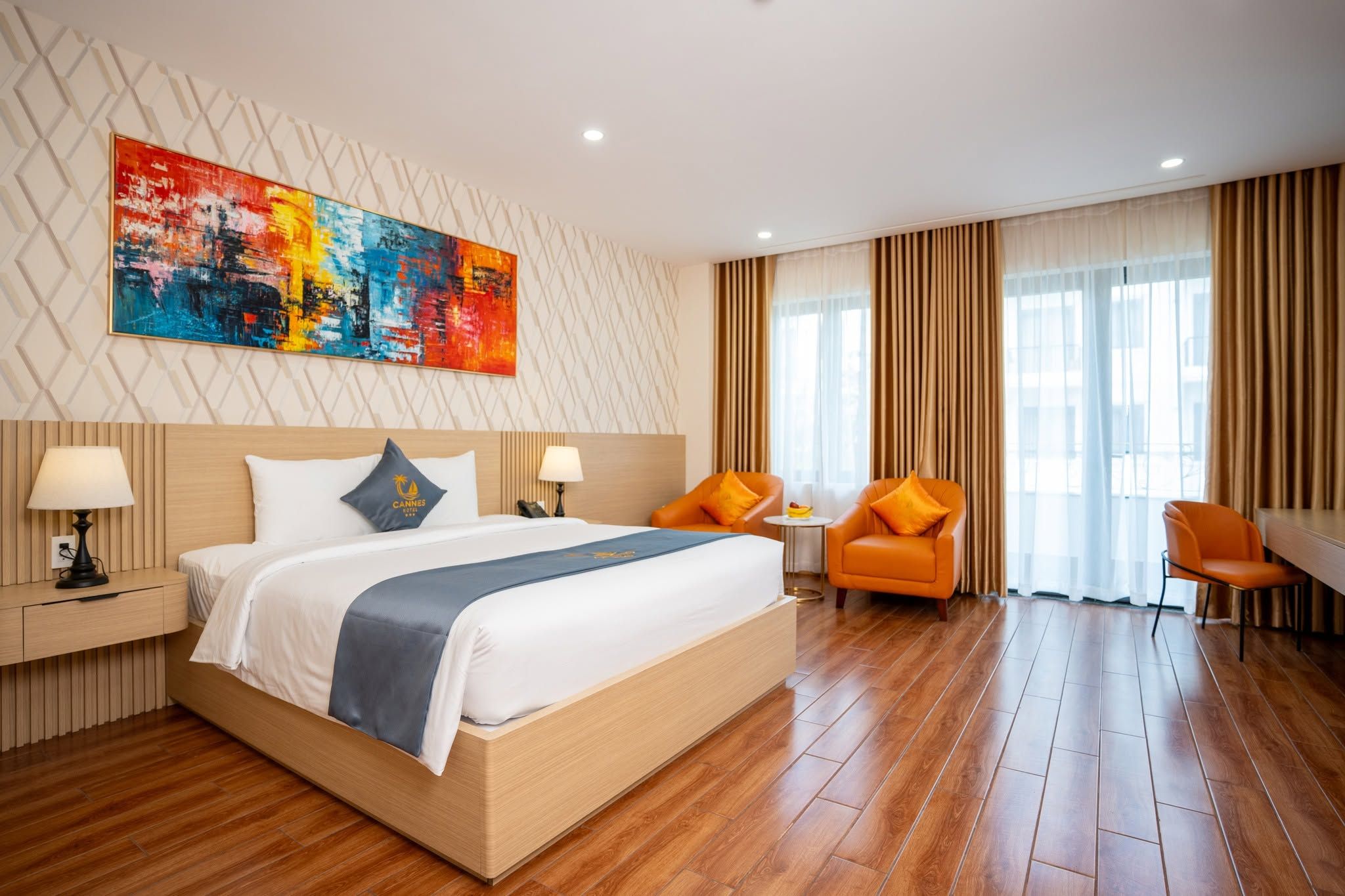 A hotel room with a bed, two chairs, a table, and a large abstract painting on the wall.