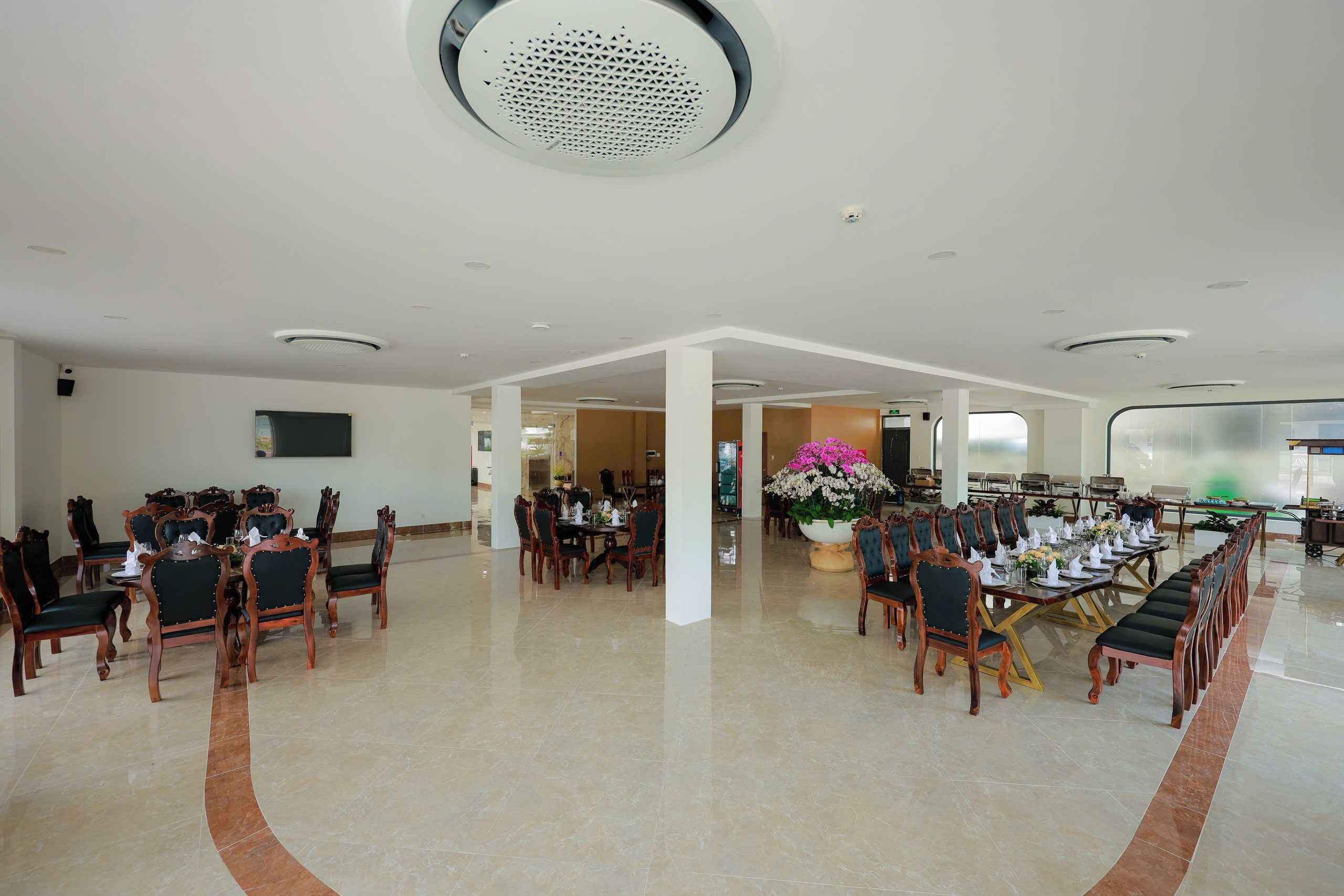 Un vaste espace dédié à la salle à manger, avec plusieurs tables et chaises, une grande plante en pot et un design moderne au niveau du plafond.
