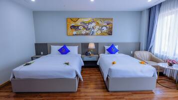 A hotel room with two beds, a nightstand, a lamp, a chair, and a painting on the wall.