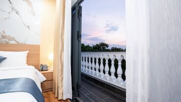 A hotel room with a bed, bedside table, lamp, and a view of a balcony with a balustrade.