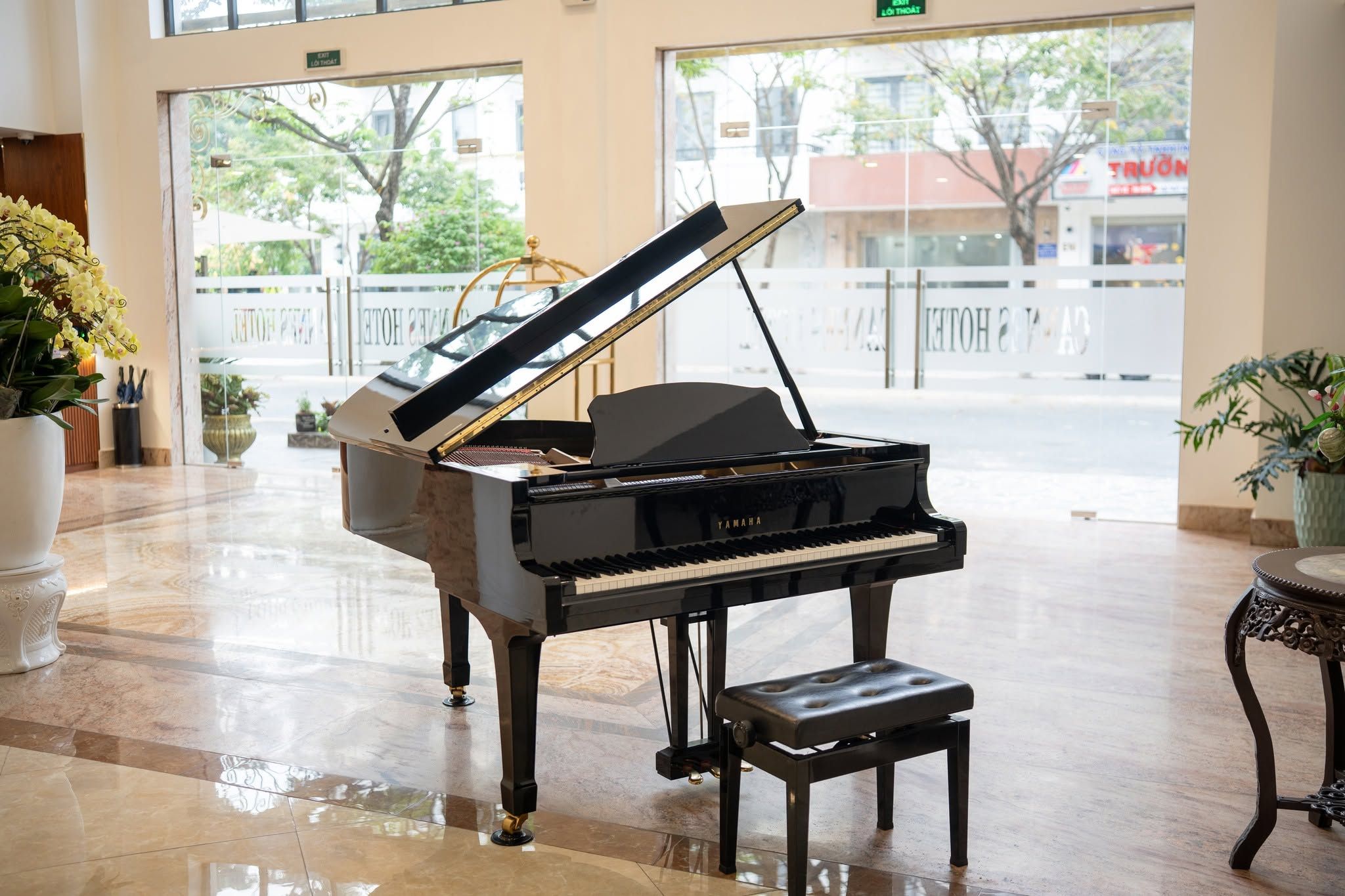 A grand piano in a spacious lobby with a marble floor, large windows, and potted plants.