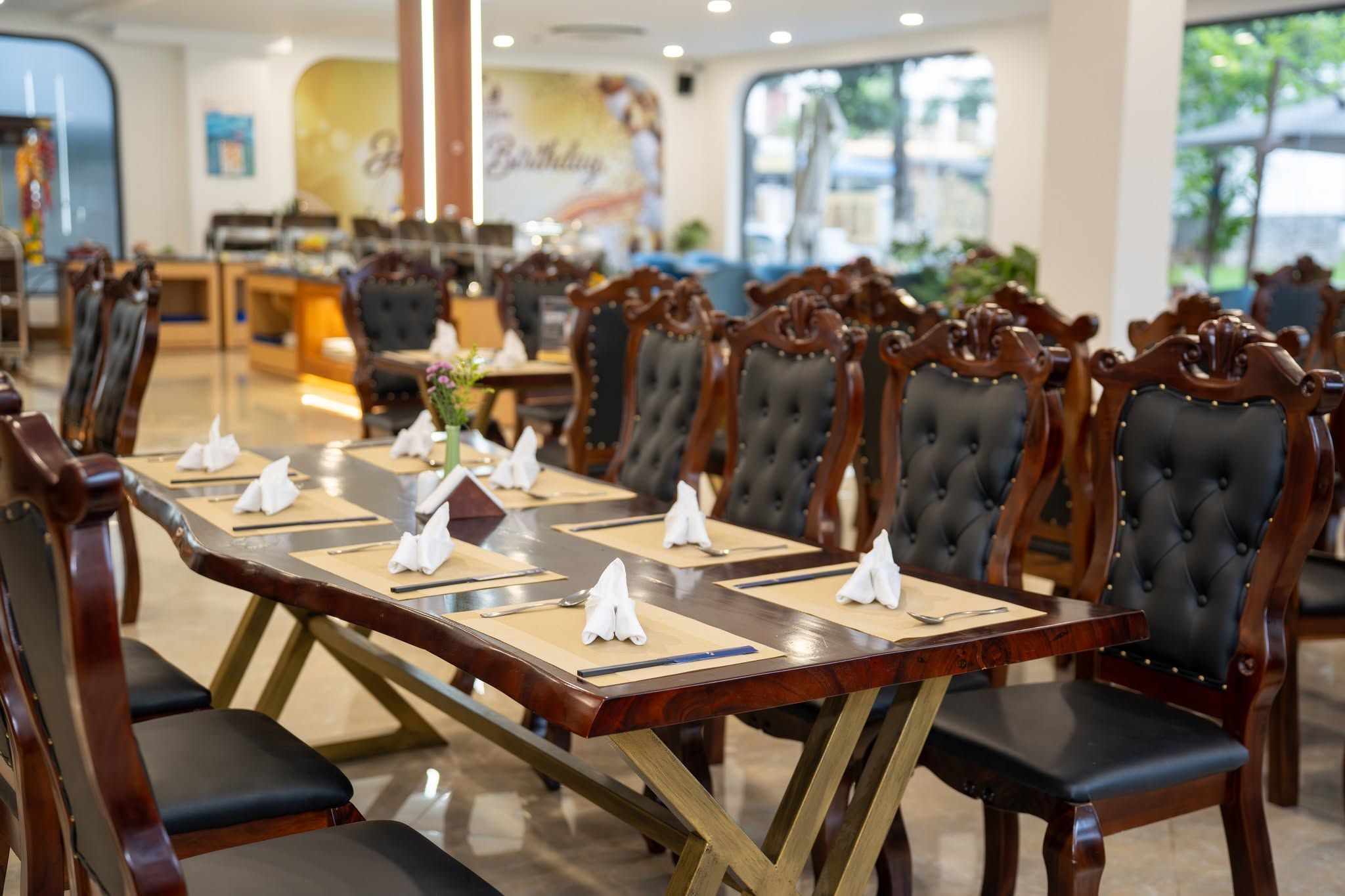 A dining area with a long table set for multiple guests, surrounded by upholstered chairs with a classic design.
