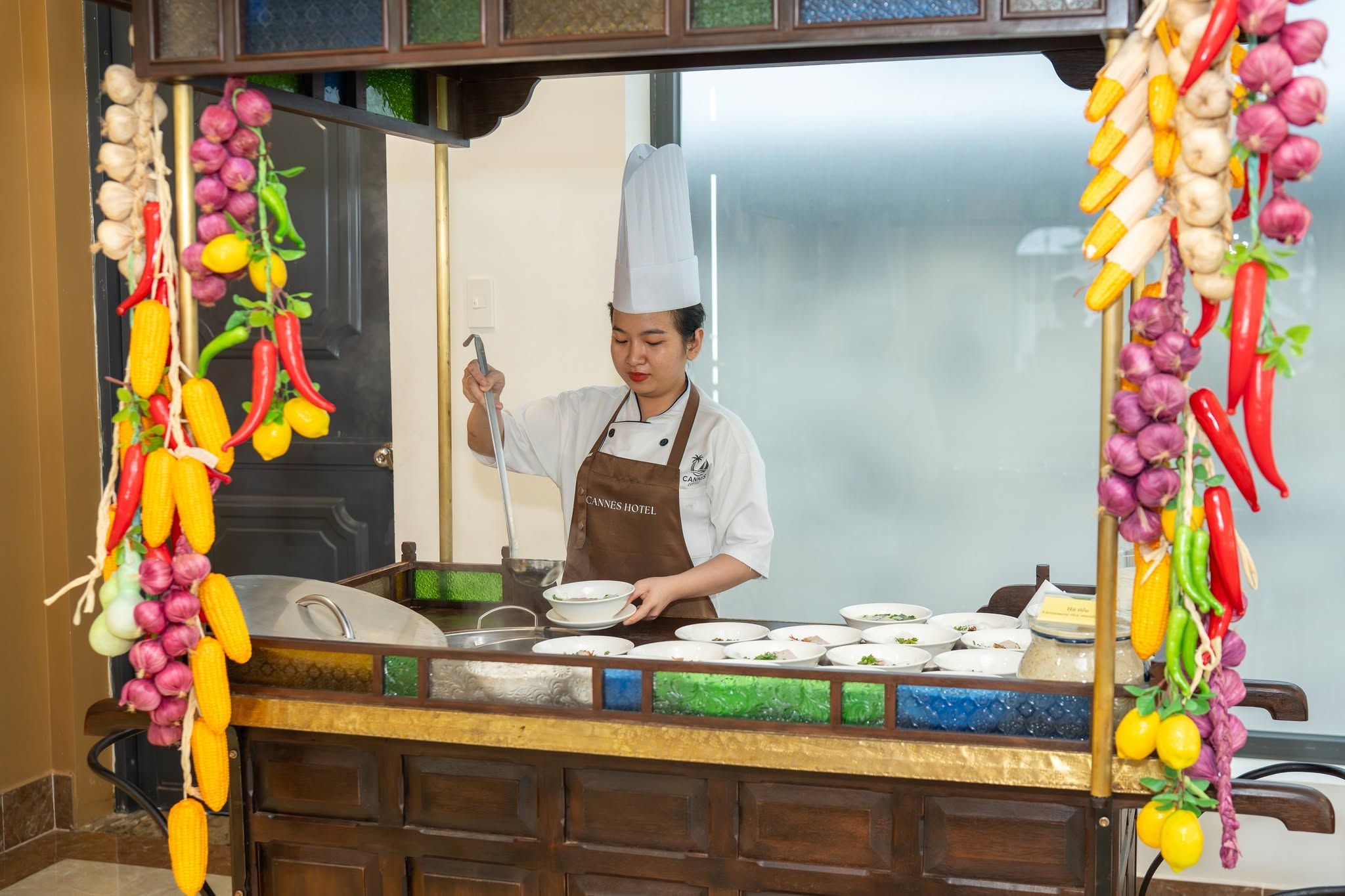A chef at a buffet counter with a variety of dishes and a decorative wall.