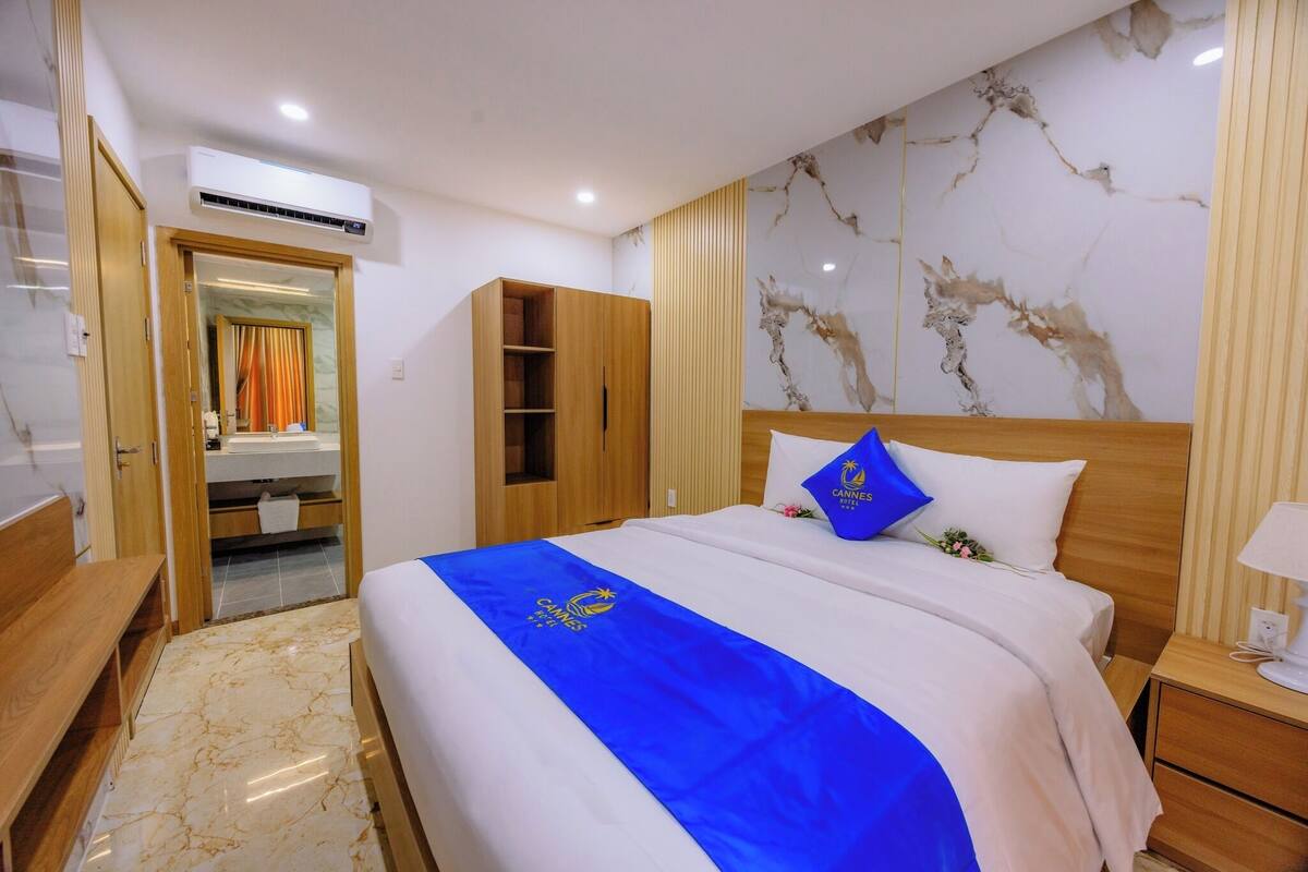 A hotel room with a bed, a wooden wardrobe, a bathroom with a mirror, and a marble-patterned wall.