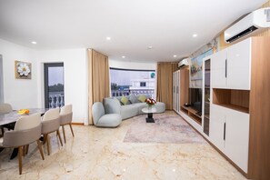 A modern living room with a sofa, dining table, and chairs, a balcony with a view, and a kitchen area with cabinets and an air conditioning unit. - Cannes Hotel (Phu Khuong)