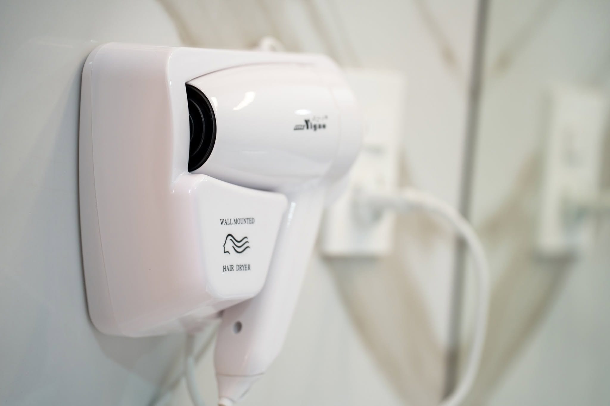 A wall-mounted hair dryer with a plug, indicating a bathroom setting.