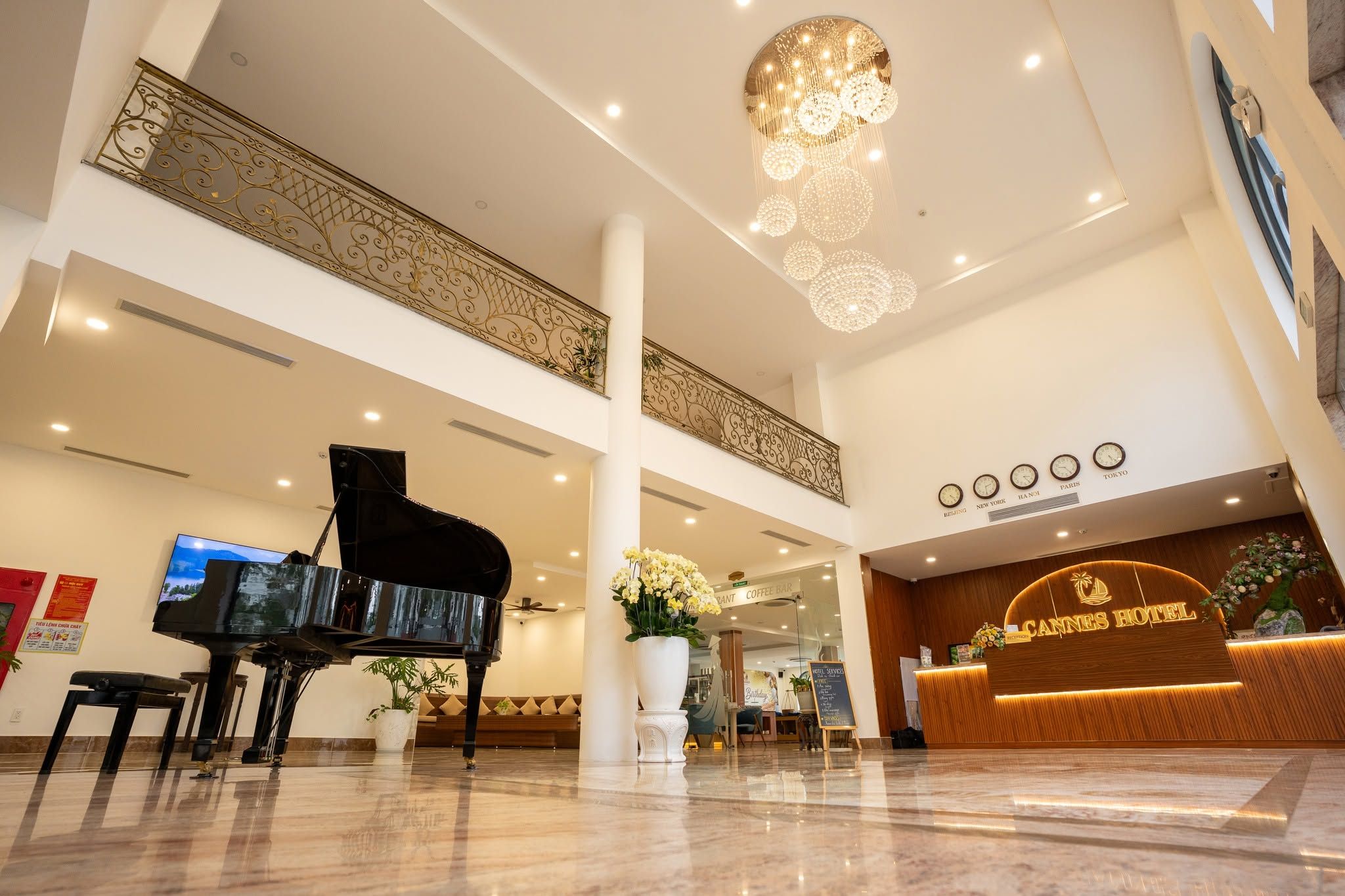 Een hotelhal met een vleugelpiano, een receptiebalie en een kroonluchter.