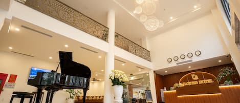 Un vestíbulo de hotel con un piano de cola, una recepción y una araña.