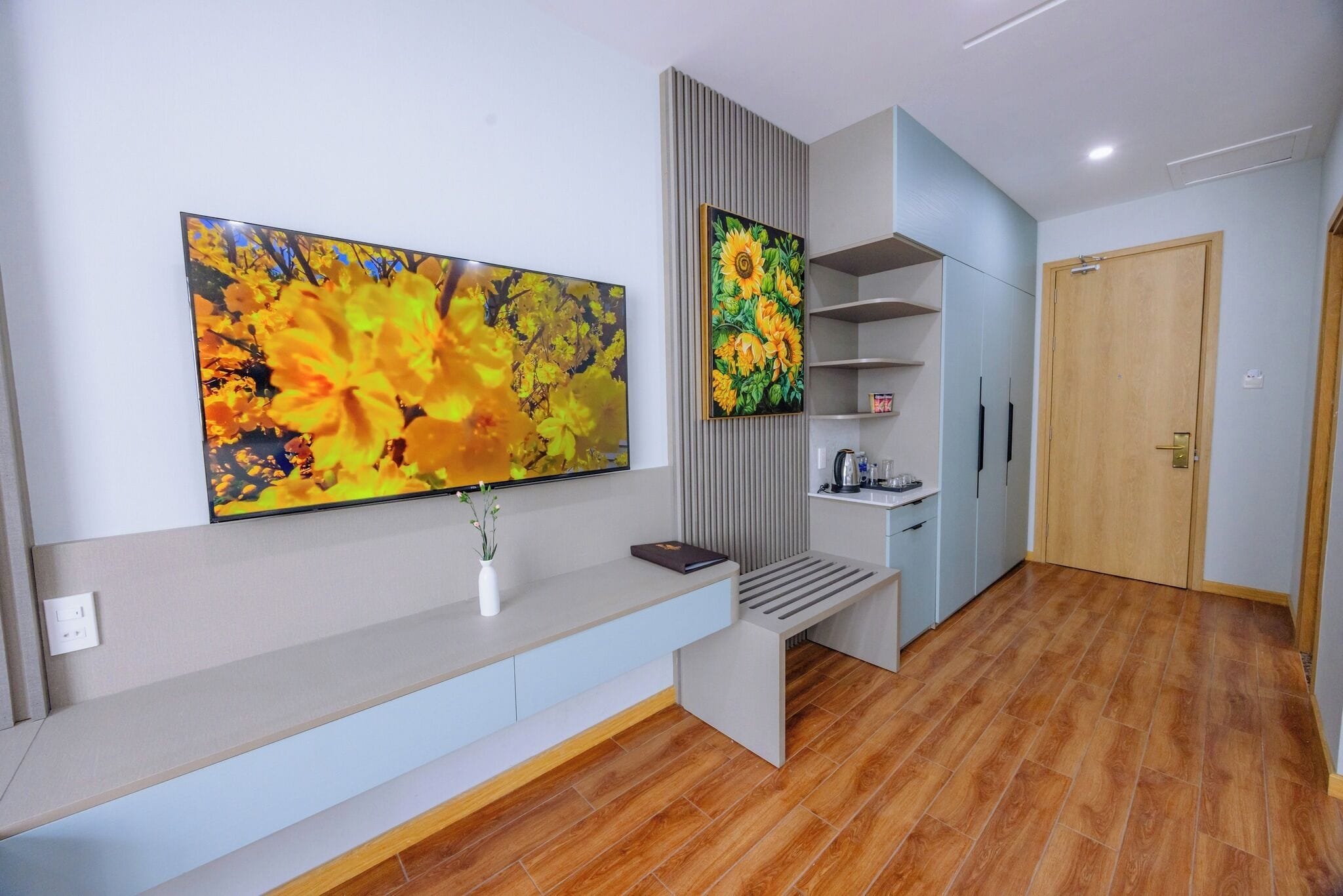 A modern hotel room with a long reception desk, a large abstract painting, a built-in shelf unit, and a wooden door.