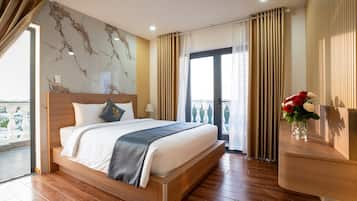 A hotel room with a large bed, a view of the city, and a balcony with curtains.
