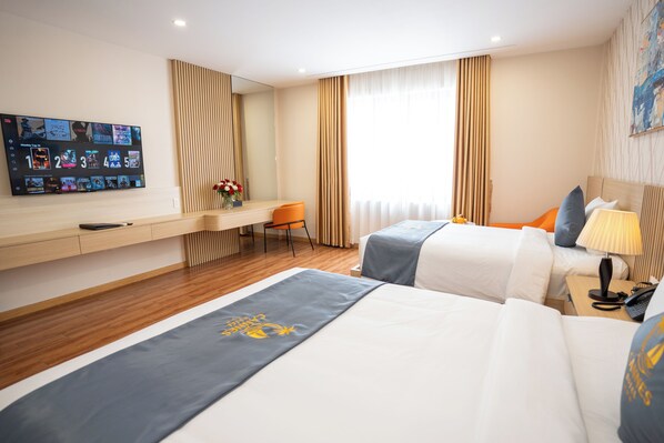 A hotel room with a bed, a desk with a computer, a chair, and a TV displaying movie options. - Cannes Hotel (Phu Khuong)