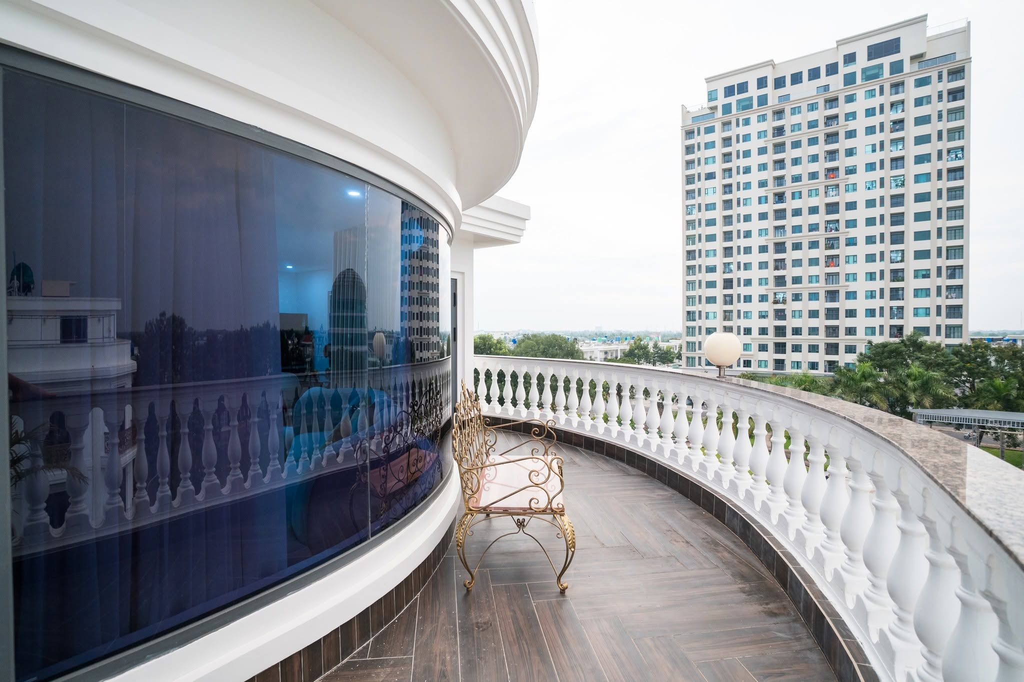 A curved balcony with a white balustrade, a metal chair, and a view of a tall building in the background.