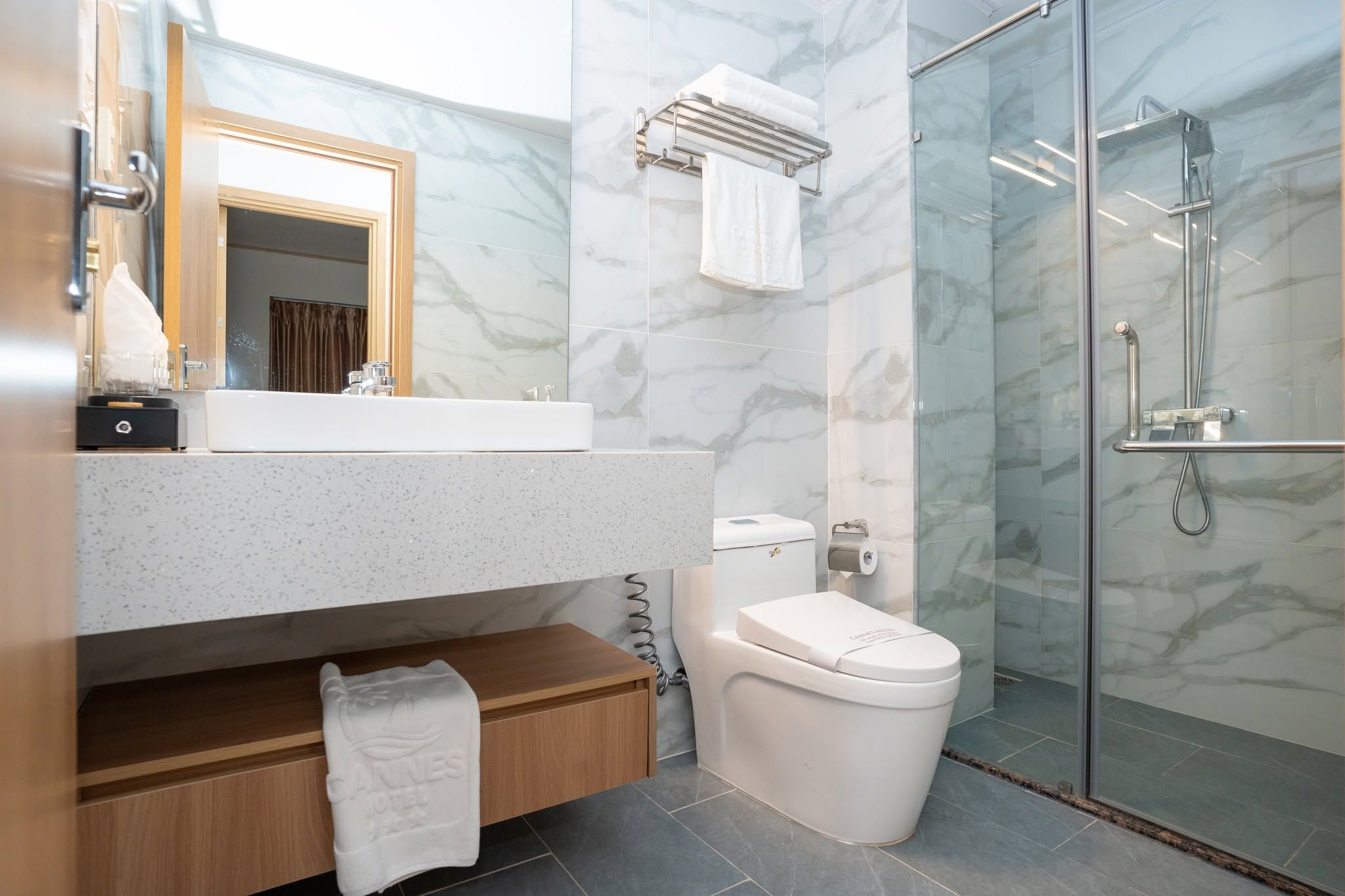 Un baño moderno con pared de mármol, cabina de ducha de vidrio y tocador de madera.