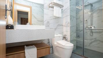 Un baño moderno con pared de mármol, cabina de ducha de vidrio y tocador de madera.