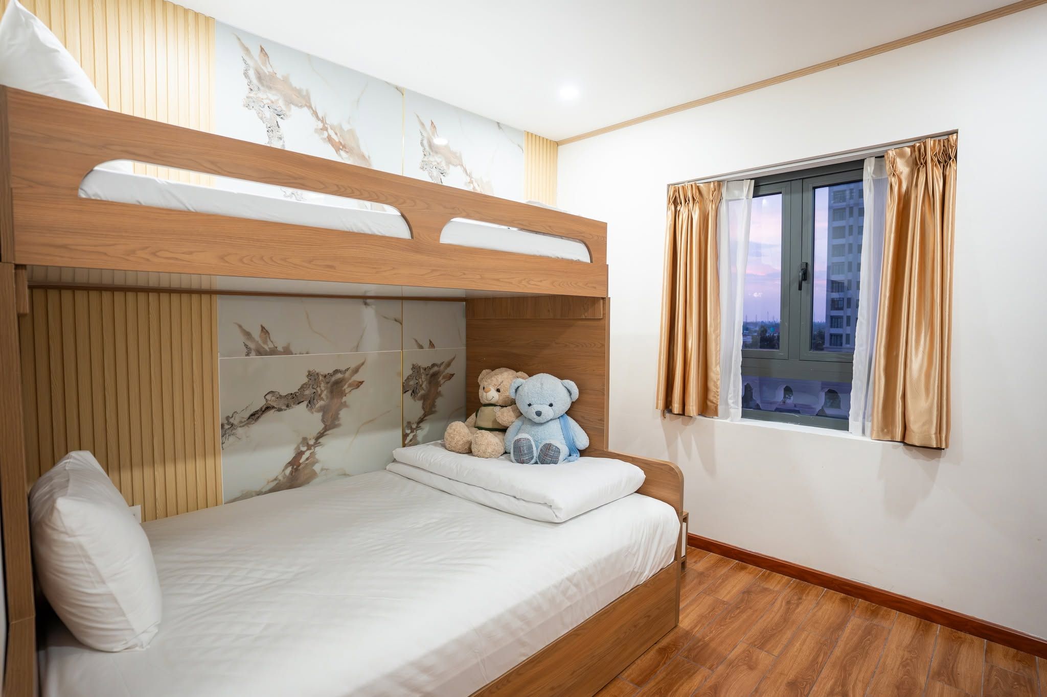 Un letto a castello con testiera in legno, una finestra con tende e un orsetto sul letto.
