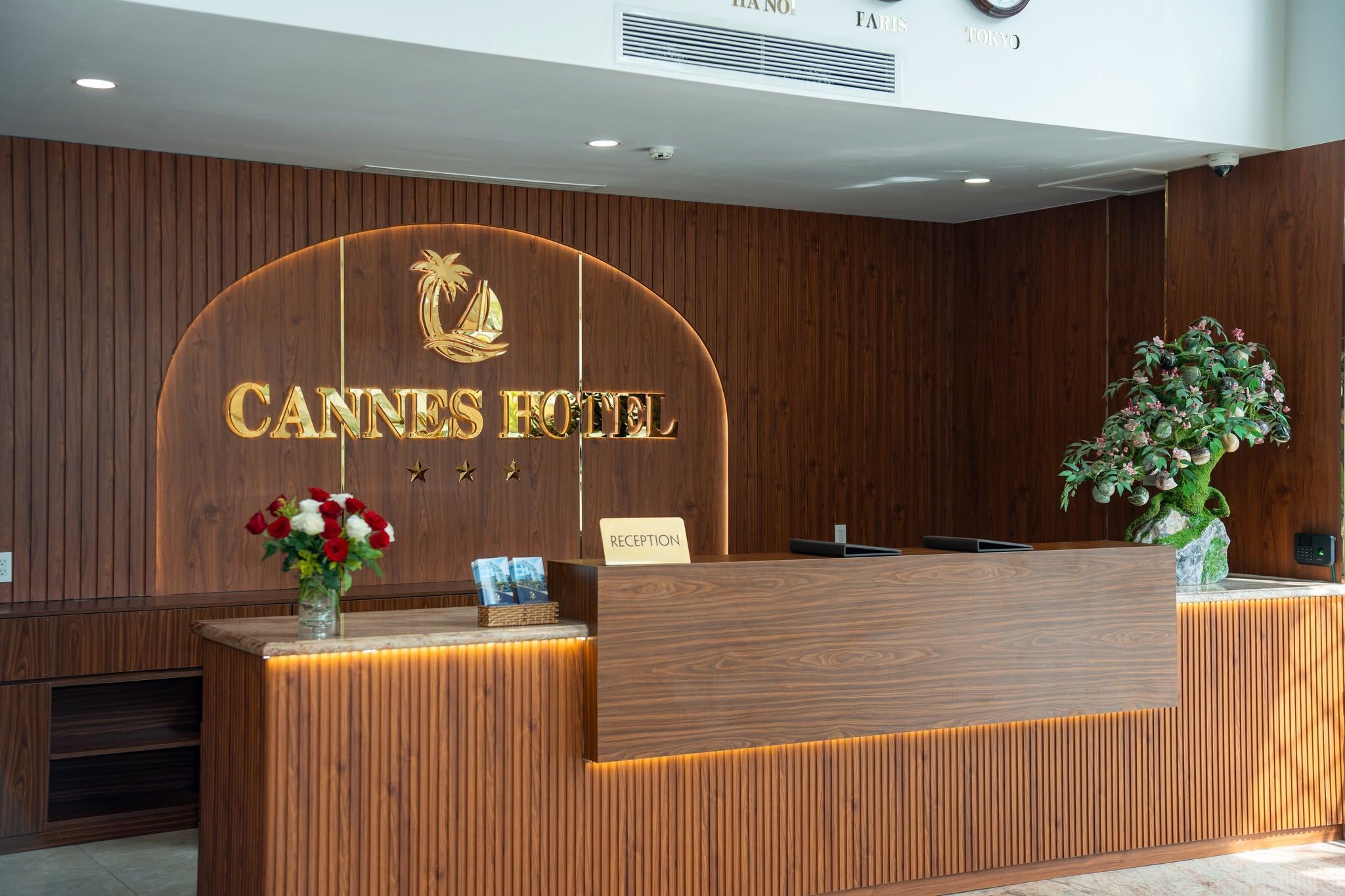 Mostrador de recepción del Hotel Cannes con detalles de madera, un letrero de recepción y una planta en maceta.