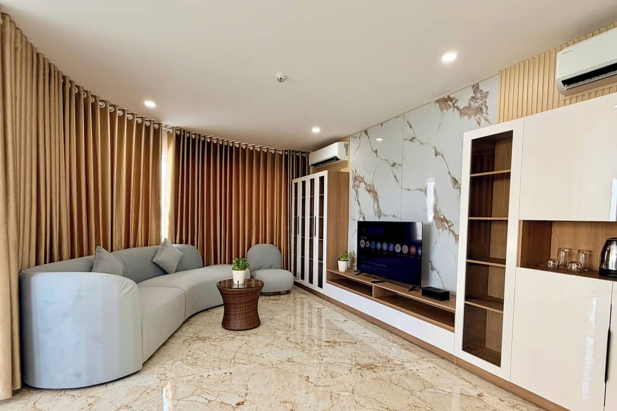 A modern living room with a curved grey sofa, a flat-screen TV mounted on a white cabinet, and a marble floor.