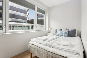 Une chambre à coucher avec un lit, une table de chevet et une fenêtre donnant sur un immeuble.