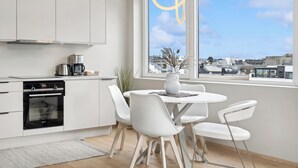A modern kitchen with white cabinetry, a built-in oven, and a dining area with white chairs and a round table. - Top apartment with high standard in the city center. Terrace and walking distance to Bryggen. (Vestland)