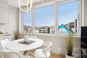 Une cuisine moderne avec des meubles blancs, une table de salle à manger ronde entourée de chaises blanches et une grande fenêtre offrant une vue sur la ville.