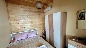 Ein Schlafzimmer mit Holzboden, einem Bett mit rosa Kissen, einem Kleiderschrank und einem Schreibtisch mit Schubladen.