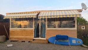 Eine Holzkonstruktion mit gestreiftem Markisenstoff und einer Tür, ein blaues Surfbrett und eine Satellitenschüssel.