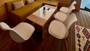 Ein gemütliches Zimmer mit Holzbalkendecke, einer Couch, einem Couchtisch und weißen Stühlen.