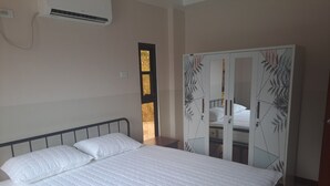 Een slaapkamer met een bed, een garderobe met een geometrisch bladpatroon en een airconditioningunit aan de muur.