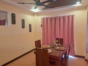 Un comedor con una mesa dispuesta para cuatro personas, un ventilador de techo y cortinas rosas.